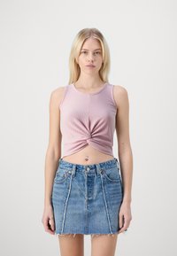 Lichtroze geribbelde crop top met gedraaide voorkant, gecombineerd met een blauwe spijkerrok met een rafelrand en vijf zakken.
