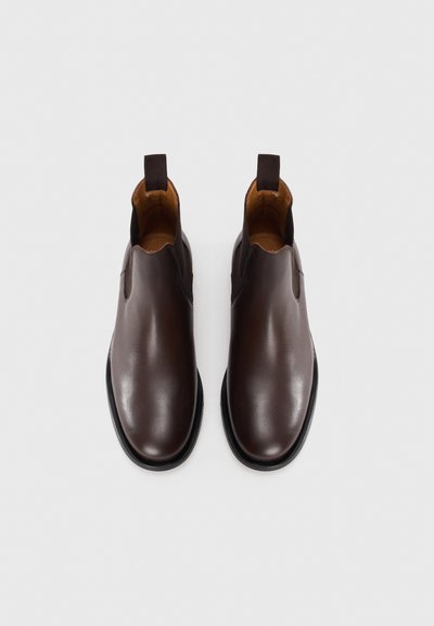 Par de botas Chelsea de cuero marrón oscuro con paneles laterales elásticos negros y lengüetas, mostradas desde arriba sobre un fondo blanco.
