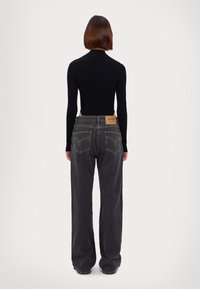 Schwarzer Ripp-Bodysuit kombiniert mit lockeren, dunkelblauen Jeans. Die Jeans haben gelbe Nähte und ein Lederpatch-Label auf der Rückseite.