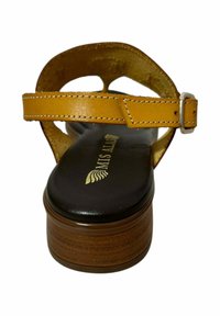 Sandalia de plataforma marrón con una correa de cuero amarillo y hebilla plateada. Cuenta con una plantilla acolchada negra con marca en relieve.