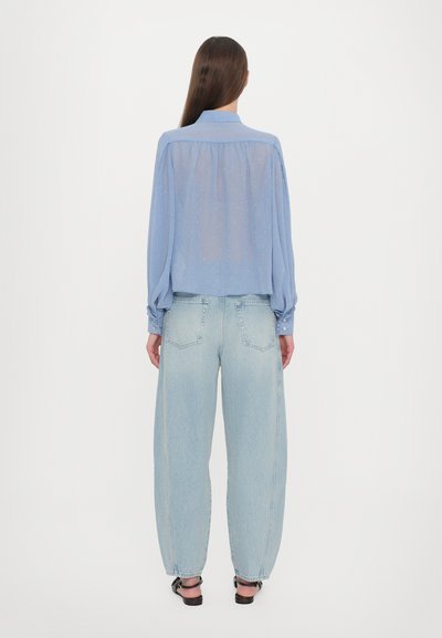 Light blue sheer blouse with gathered back detail and buttoned cuffs, paired with high-waisted, loose-fitting light denim jeans.