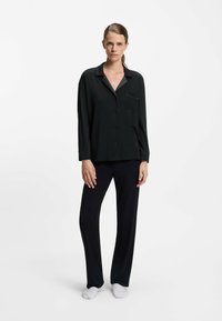 Black pajama set featuring a button-up shirt with a chest pocket and long sleeves, paired with loose-fitting, matching pants. Soft fabric texture.
