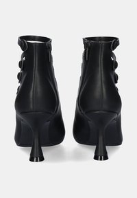 Botas de tobillo de cuero negro con punta afilada, tacón de aguja alto y botones decorativos. Con cierre de cremallera en la parte trasera.