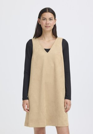 Beige suede dress with a V-neckline and loose fit, layered over a black long-sleeve top. Smooth texture and straight hemline.