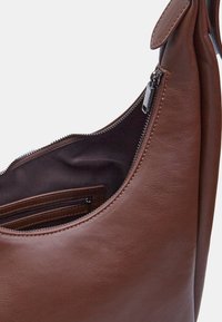 Braune Leder-Schultertasche mit glatter Textur, geschwungenem Design, einem oberen Reißverschlussverschluss und einer Innentasche mit zusätzlichem Reißverschlussdetail.