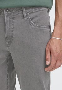 Szürke farmernadrág öt zsebes kialakítással. Jellemzői a klasszikus gombos záródás, finom varrás és puha tapintás.