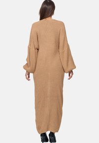 Lång, stickad cardigan i beige med ett strukturerat mönster, som har vida ärmar och en avslappnad passform, som når ner till anklarna.