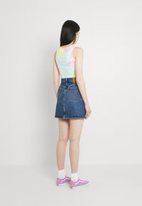 Top sin mangas tie-dye en colores pastel, falda mini de mezclilla y zapatillas Vans rosas con calcetines blancos. Textura destacada y estilo casual.