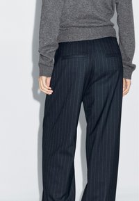 Marineblau gestreifte Hosen aus strukturiertem Stoff, mit hohem Bund, seitlichen Taschen und geradem Bein. Grauer Pullover teilweise sichtbar.