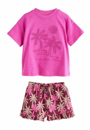 Camiseta rosa de manga corta con diseño en relieve de palmera y sol, combinada con pantalones cortos marrones que presentan patrones de palmeras en rosa y beige, y dobladillos con volantes.