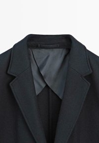 Tmavě vlněný blazer s límcem a hladkým šedým saténovým podšívkou, vyznačující se klopou s výstřihem a čistým, strukturovaným designem.