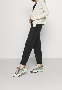 Beige stickad cardigan, svarta tapered jeans och mönstrade gröna och vita sneakers med tjock sula, med snörningsdesign och accenter.