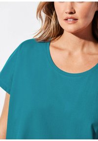 Ein türkisfarbenes Kurzarmshirt mit rundem Halsausschnitt, aus einem glatten Stoff gefertigt, der ein sauberes, einfaches Design ohne Muster oder Akzente aufweist.