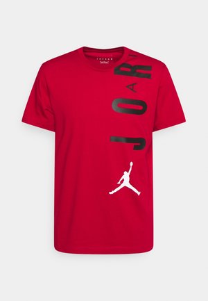 T-shirt rouge en coton avec un imprimé vertical noir "JORDAN" et un logo Jumpman blanc en bas à droite. Manches courtes, design col rond.