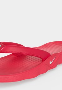 Κόκκινο σανδάλι Nike flip-flop με υφή στο πέλμα, μαλακό λουράκι και λευκό λογότυπο Nike swoosh στο πλάι.
