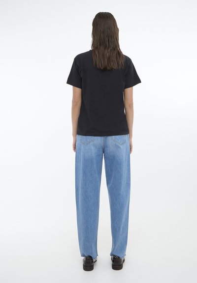 Tricou din bumbac negru cu mâneci scurte, purtat cu blugi decolorati cu croi larg. Cusături vizibile pe spate și croi lejer, completat cu pantofi negri.