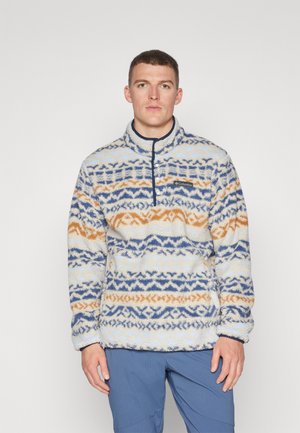 Kohvikleidiga fliispusa kõrge kraega, millel on kreemivalgel taustal sinine ja oranž geomeetriline muster, rinna peal brändi logo.