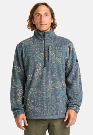 Fleece pullover in blauwe en groene tinten met een geometrisch patroon, ritssluiting bij de hals en een textuurfinish. Lange mouwen met elastische manchetten.