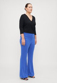 Haut noir à manches trois-quarts associé à un pantalon bleu taille haute et à jambes larges, avec un détail de bouton sur le devant et une texture lisse.