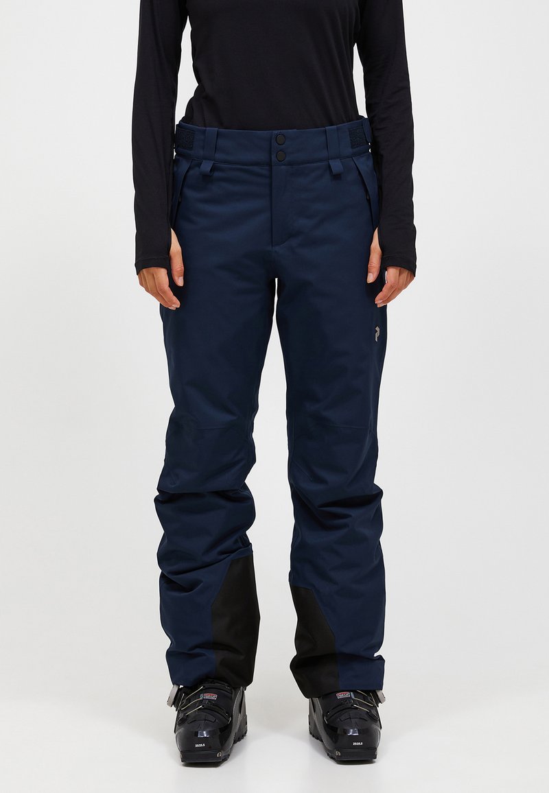 Marineblå vandtætte skibukser med høj talje, to frontknapper og sorte detaljer ved anklerne. Stoffet er glat og struktureret.