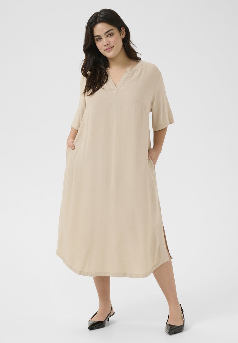 Robe beige mi-longue avec des manches courtes, décolleté en V, poches latérales et coupe décontractée. Texture lisse et fentes sur les côtés près de l'ourlet.