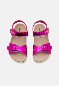 Pari di sandali metallici fucsia per bambini con cinturini regolabili alla caviglia e cinturini anteriori con fibbia su suole beige.
