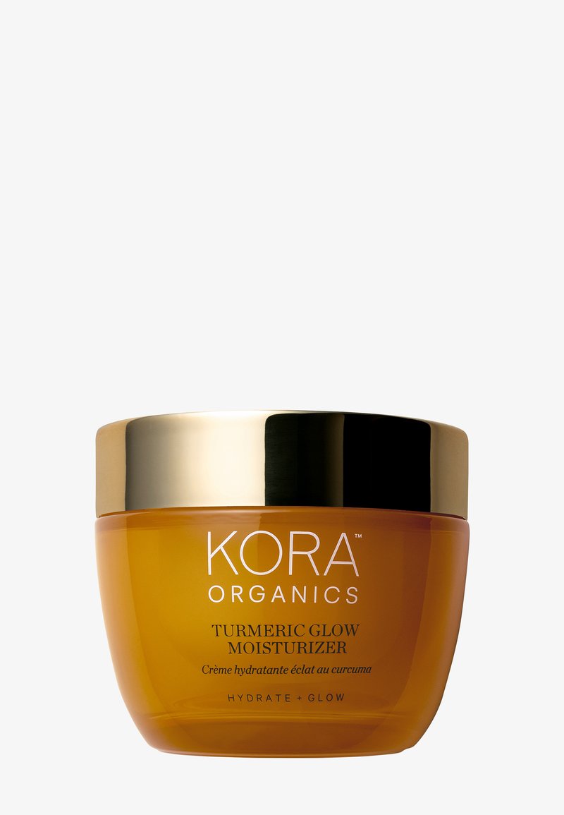 Bocal en verre orange avec un couvercle doré, étiqueté "KORA Organics Crème Hydratante Éclat au Curcuma" en texte blanc. Texture lisse, forme ronde.