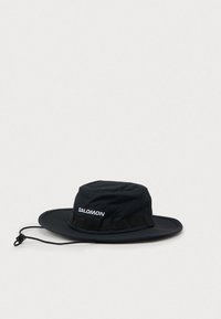 Chapéu Salomon outdoor de aba larga e preta, com fita ajustável no queixo e ilhós de ventilação em tecido, sobre um fundo simples.