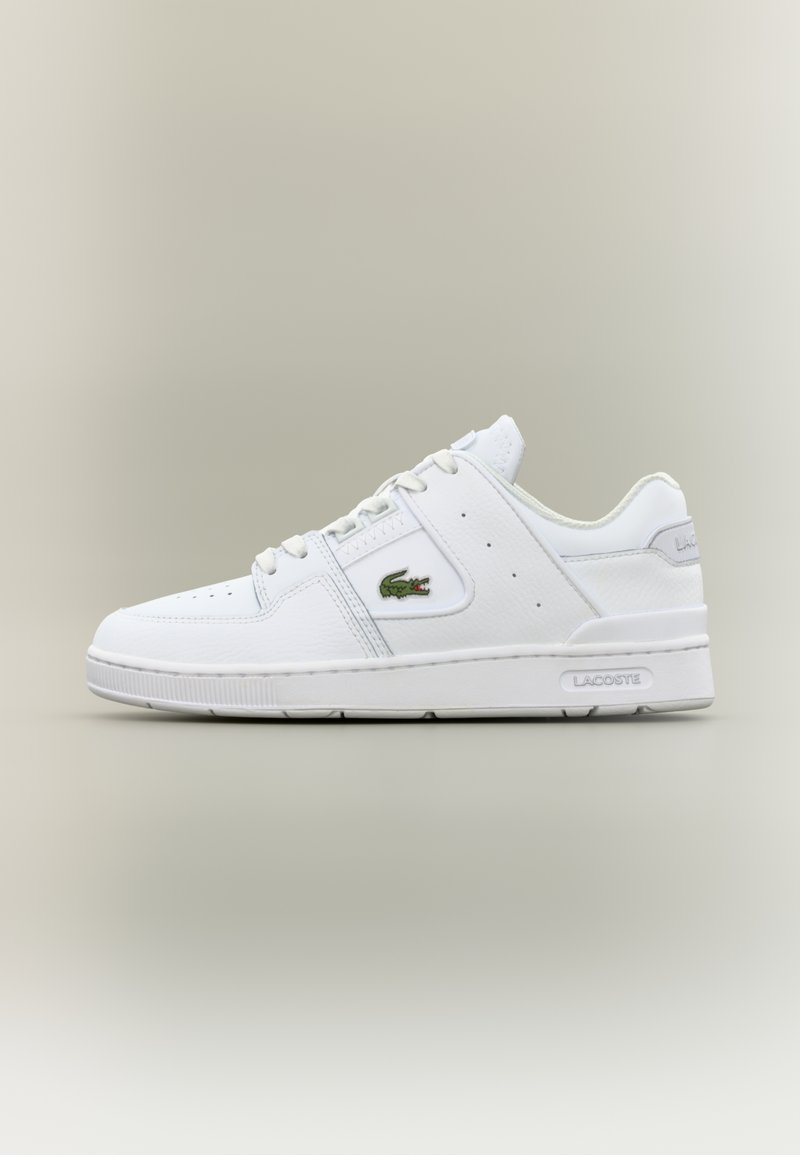 Białe skórzane sneakersy o gładkiej fakturze, okrągłym nosku, perforowanych detalach, zielonym logo krokodyla oraz brandingiem "Lacoste" z boku.