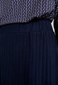 Námořnická plisovaná sukně s texturovaným povrchem, disponující širokým pasem a vertikálními pruhy. Tkanina má jemný vzhled, ideální pro vrstvení.
