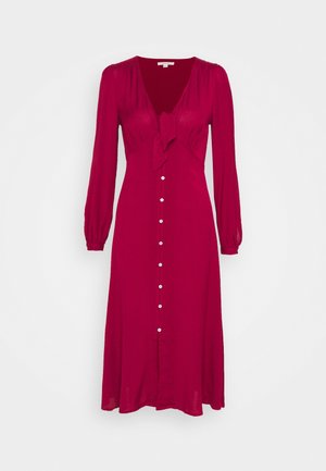Robe midi rouge à manches longues avec un décolleté en V profond, un détail volanté, une fermeture boutonnée devant et des poignets froncés sur fond blanc uni.