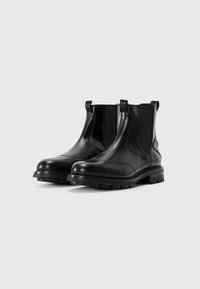 Las botas de tobillo de cuero negro presentan un acabado suave y brillante, paneles laterales elásticos y suelas de goma robustas con un dibujo texturizado para mayor agarre.