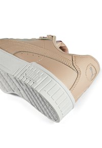Baskets Puma beige inclinées pour montrer la semelle texturée détaillée, la semelle intermédiaire blanche avec le logo Puma et le logo cousu sur l'onglet du talon.