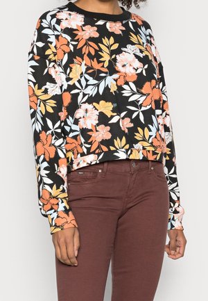 Black long-sleeve floral top with orange, yellow, and white flowers paired with dark brown fitted pants on a standing person.
