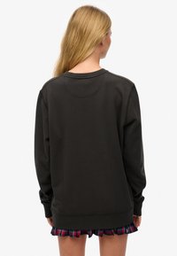 Felpa nera con maniche lunghe, polsini a coste e scollo rotondo, abbinata a una minigonna a quadri. Vista posteriore, con una texture liscia.