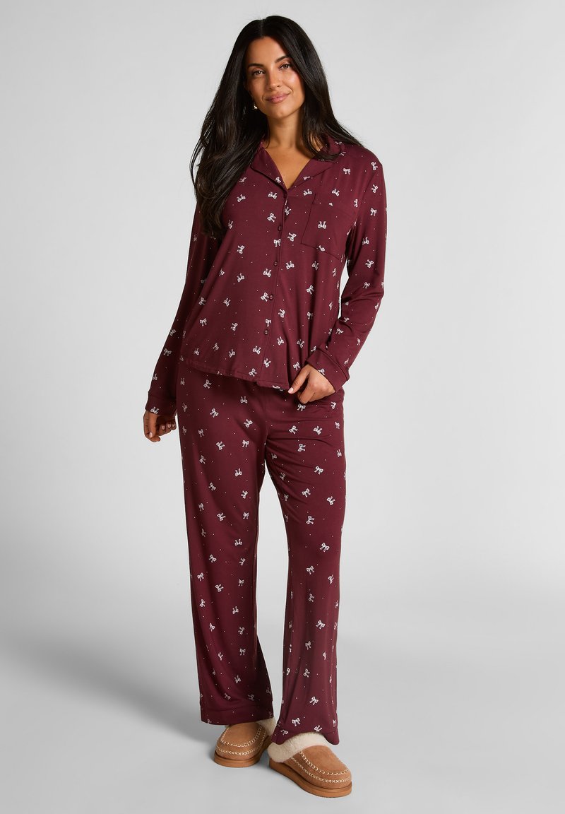 Bordeaux pajama set met lange mouwen en broek, voorzien van een wit patroon. Het materiaal lijkt zacht, met een relaxte pasvorm en knoopsluiting aan de voorkant.
