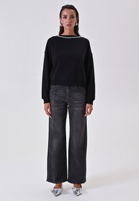 Felpa nera accorciata con scollatura decorata, abbinata a jeans neri a vita alta e a gamba larga e scarpe con dettaglio a fiocco argento.