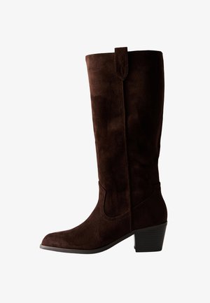 Botte en daim marron haute jusqu'au genou avec un bout pointu et un talon bas empilé. Présente une couture décorative et un détail de couture le long de la tige.