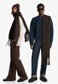 To modeller bærer tøj: en løstsiddende cremefarvet sweater, et mørkebrun tørklæde med frynser, mørkebrun bukser og en fuzzy blå sweater med denim.