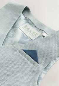 Lichtgrijs gestructureerd vest met een voering met bloemmotief, gelabeld "Baker by Ted Baker," voorzien van een gevouwen marineblauw pochet.