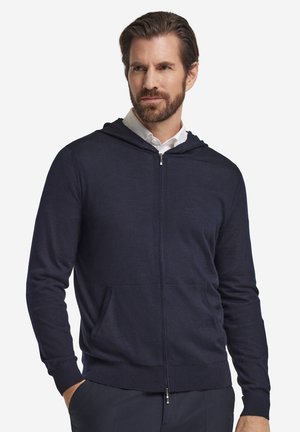 Marineblå hættejakke med lynlås lavet af blødt stof med snøre, forlommer og ribstrikkede manchetter, der har et enkelt, rent design.