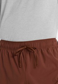 Pantalones cortos marrones cortos con una cintura elástica, que cuentan con un cordón y un patrón de superficie texturizado, combinados con una camisa gris claro.