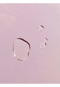 Transparent water droplets on a soft pink surface, varying in size and shape, with smooth edges and subtle reflections.
