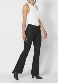 Pantalones acampanados negros con un patrón floral, hechos de una tela texturizada, combinados con una blusa sin mangas blanca y botas de tacón negro.