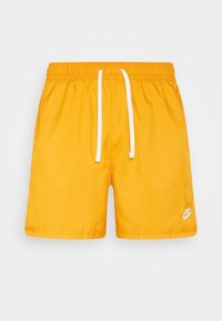 Krótkie spodenki do pływania Nike w jasnym żółtym kolorze, z elastycznym pasem w talii i białym sznurkiem do regulacji oraz małym białym logo w prawym dolnym rogu.