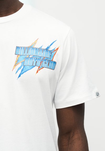 Λευκό μπλουζάκι με μπλε και πορτοκαλί γραφικό κείμενο "Billionaire Boys Club" στο στήθος, που φοριέται από άτομο με καφέ επιδερμίδα, ορατή από τον λαιμό μέχρι το μέσο του βραχίονα.