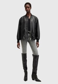 Zwarte leren bomberjack met ribgebreide details, gecombineerd met grijze high-waisted jeans en kniehoge zwarte leren laarzen.