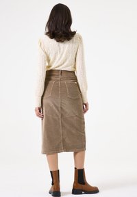 Gebreide crèmekleurige trui met een tekstuurpatroon, gecombineerd met een bruin corduroy midi-rok met achterzakken, en bruine enkellaarsjes met zwarte zijkanten.