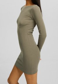 Robe à manches longues, côtelée, de couleur vert olive avec une silhouette ajustée et un col rond. Elle présente une texture lisse et une longueur mini.