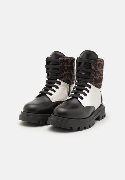 Bottines en cuir noir et blanc avec une semelle épaisse, présentant un empeigne en tissu marron à motifs et des lacets noirs.